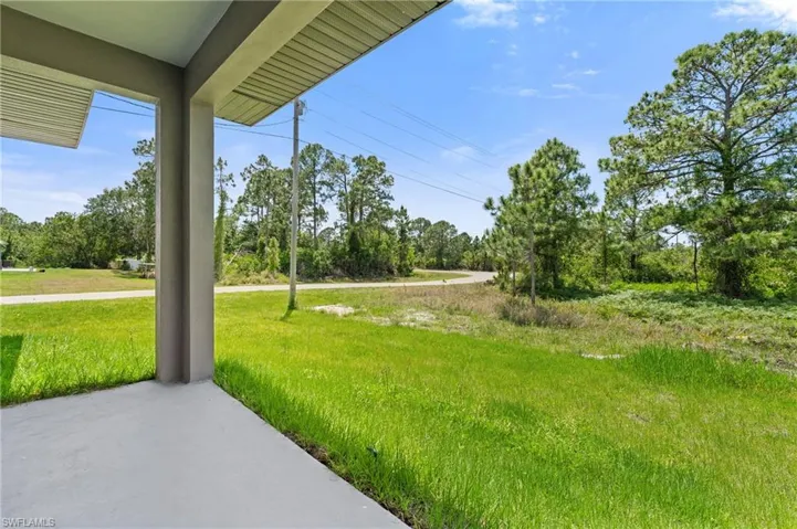 View of green lawn featuring view of wooded area and a porch