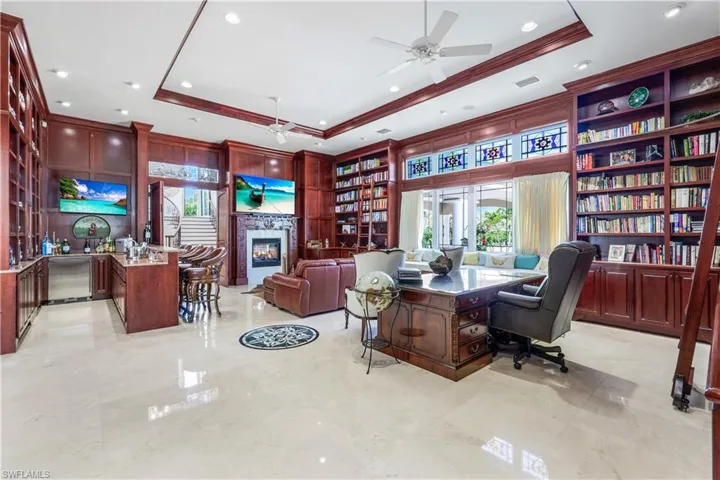 Office area with a tray ceiling, ceiling fan, a glass covered fireplace, crown molding, and recessed lighting