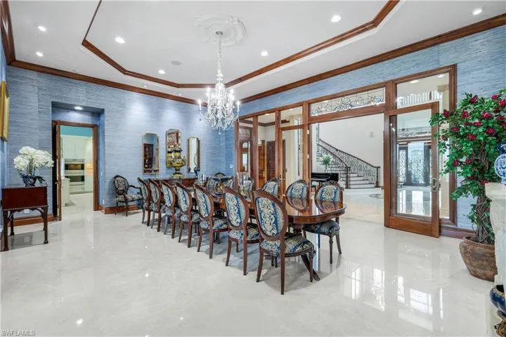Dining area with wallpapered walls, a raised ceiling, stairway, ornamental molding, and a chandelier