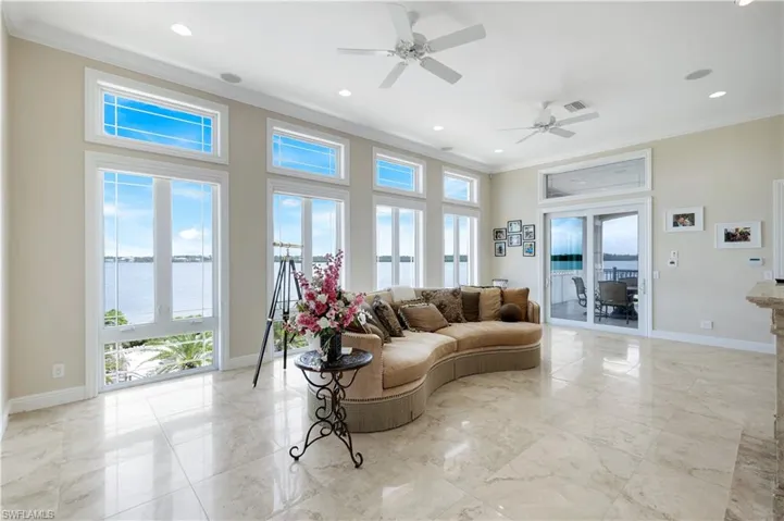 Living area off the primary bedroom featuring crown molding, a water view, light marble finish floors, a ceiling fan, and recessed lighting