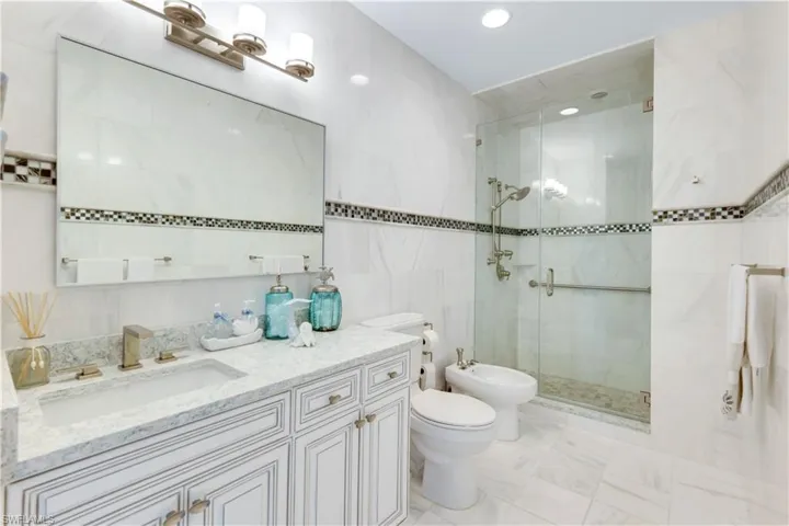 Full bath with tile walls, a bidet, vanity, a stall shower, and recessed lighting