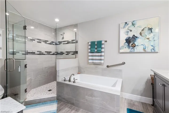 Bathroom with vanity, a garden tub, a stall shower, wood finished floors, and recessed lighting