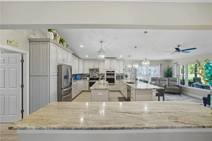 Kitchen with backsplash, decorative light fixtures, light stone countertops, open floor plan, and stainless steel appliances