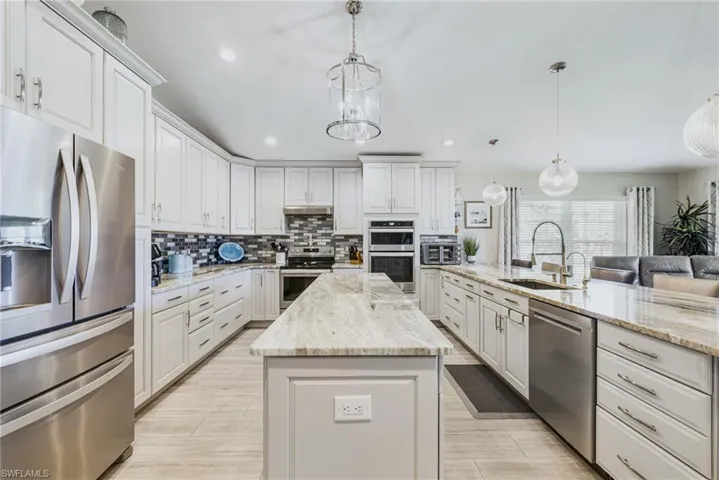 Kitchen featuring appliances with stainless steel finishes, backsplash, a center island, light stone countertops, and pendant lighting