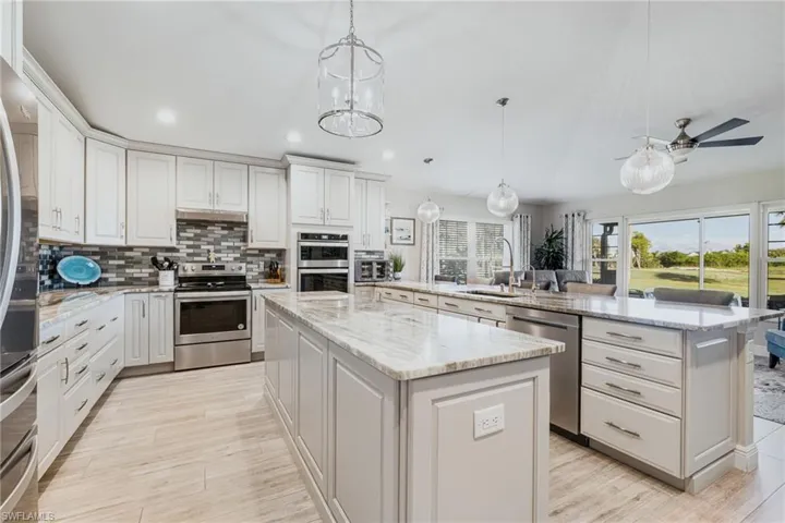 Kitchen with tasteful backsplash, stainless steel appliances, decorative light fixtures, light stone counters, and white cabinets