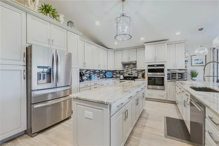 Kitchen with appliances with stainless steel finishes, decorative backsplash, light stone countertops, hanging light fixtures, and a kitchen island