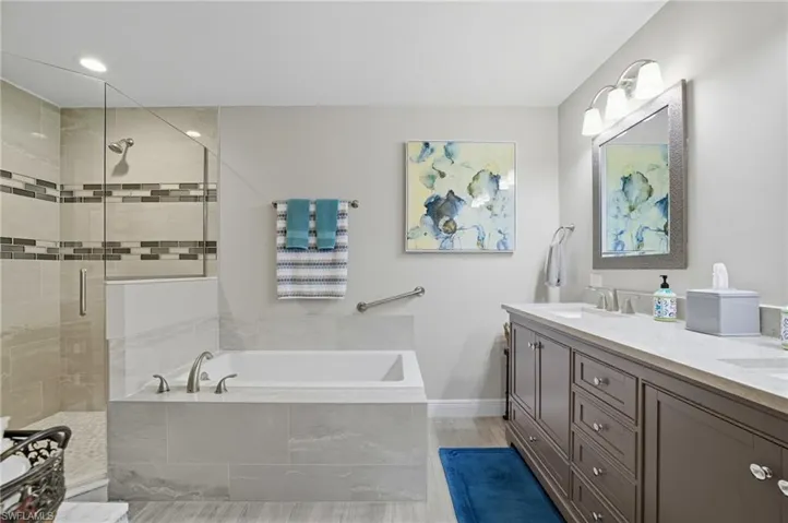 Bathroom with a garden tub, double vanity, a stall shower, light wood finished floors, and recessed lighting