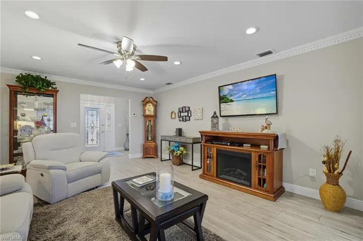 Living room with light wood-style floors, ornamental molding, a ceiling fan, a fireplace, and recessed lighting