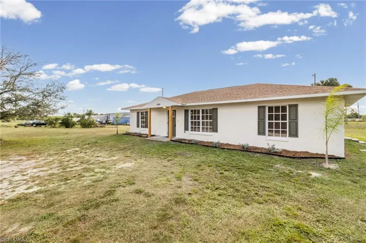 View of front of property featuring a front yard, stucco siding, and roof with shingles