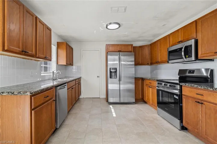 Kitchen with appliances with stainless steel finishes, dark stone countertops, decorative backsplash, and brown cabinets