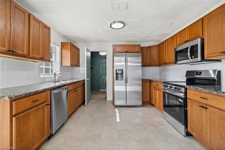 Kitchen featuring appliances with stainless steel finishes, tasteful backsplash, dark stone countertops, and brown cabinetry