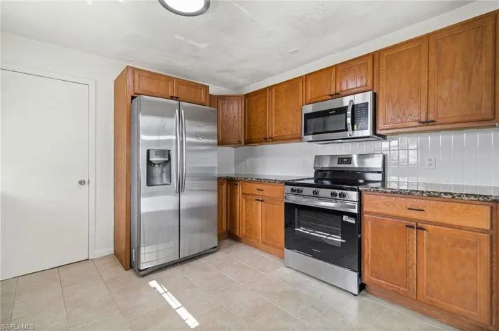 Kitchen featuring stainless steel appliances, dark stone countertops, brown cabinetry, and backsplash