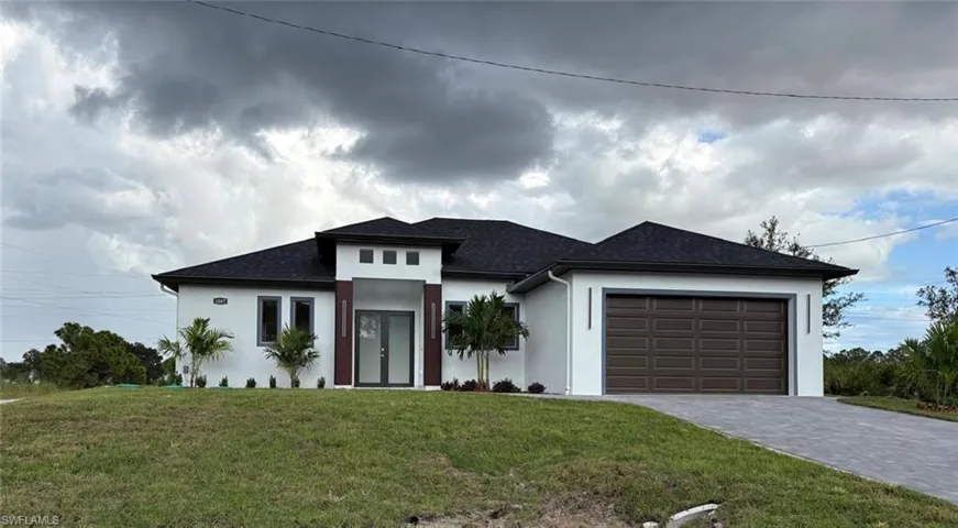 Prairie-style home with a front yard, stucco siding, decorative driveway, an attached garage, and roof with shingles