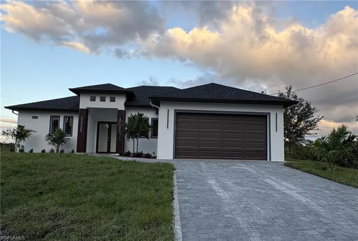 Prairie-style home featuring stucco siding, a front yard, decorative driveway, and an attached garage