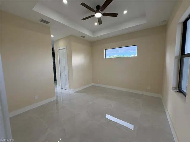 Unfurnished room with a raised ceiling, recessed lighting, ceiling fan, and light marble finish flooring
