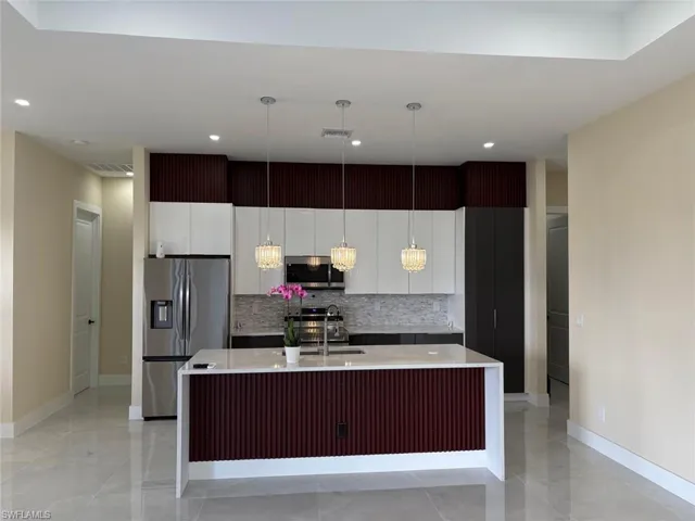 Kitchen with a kitchen island with sink, hanging light fixtures, modern cabinets, light stone countertops, and appliances with stainless steel finishes