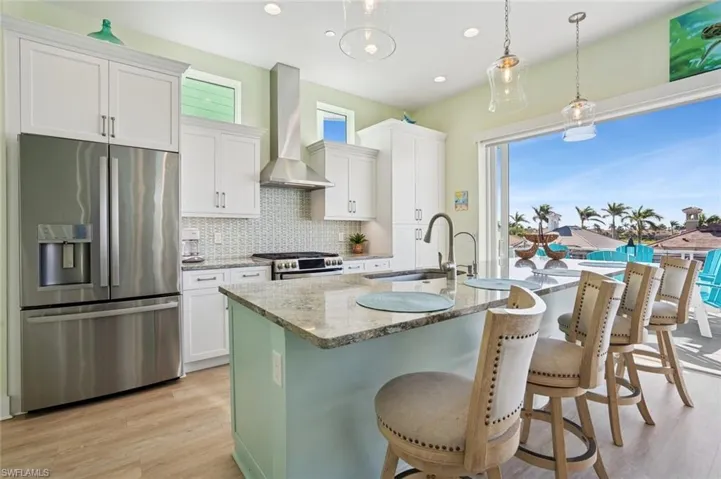 Kitchen with a breakfast bar Island, sink, tile backsplash, stainless steel appliances, and wall chimney range hood