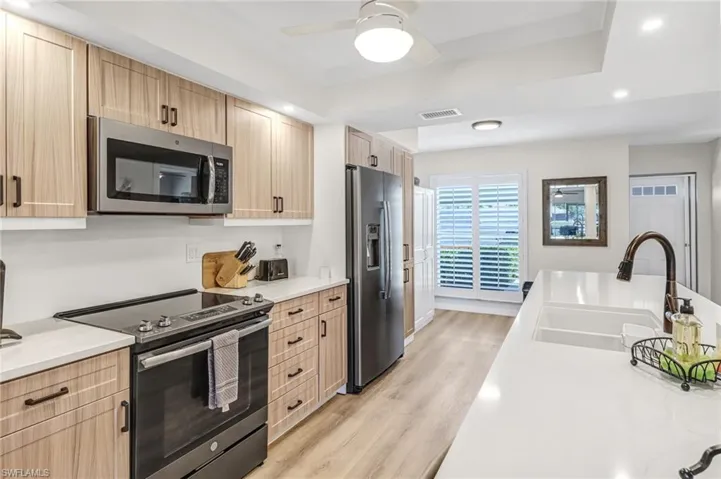 Kitchen with light hardwood / wood-style floors, appliances with stainless steel finishes, sink, ceiling fan, and light brown cabinetry