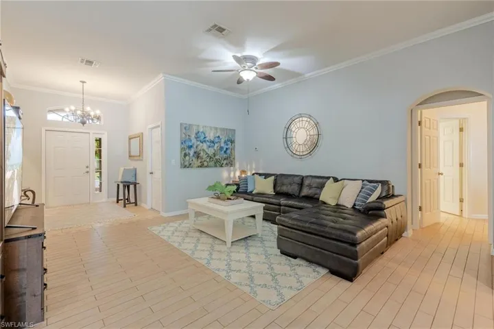 Living room with ornamental molding and ceiling fan. Tile floor throughout.