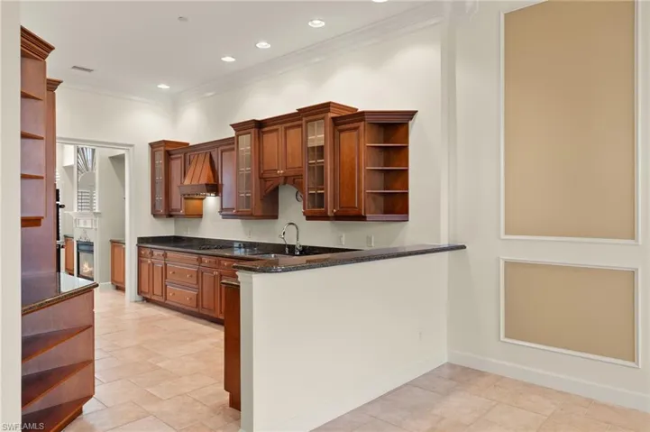 Kitchen featuring kitchen peninsula, dark stone countertops, wall chimney range hood, ornamental molding, and sink