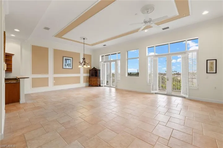 Expansive, Upscale  Living & Dining room featuring a healthy amount of sunlight through Glass Doors & large Picture Window, ceiling fan with notable chandelier, Plantation Shutters and a tray ceiling