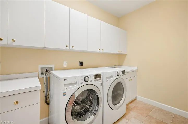 Clothes washing area with cabinets, light tile patterned floors, separate washer and dryer, and sink