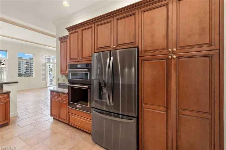 Kitchen with stainless steel fridge, double oven, crown molding, and dark stone counters