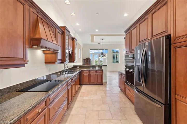 Kitchen with decorative light fixtures, dark stone countertops, black electric stovetop, stainless steel fridge with ice dispenser, and ornamental molding