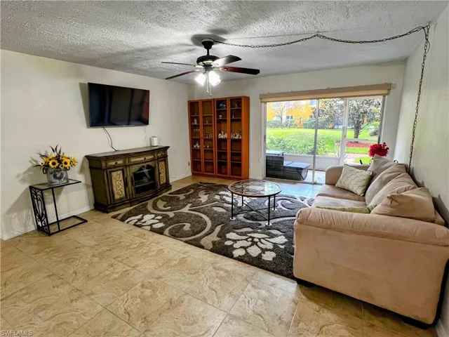 Living room with ceiling fan, a textured ceiling, and a fireplace