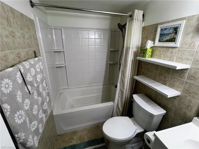 Full bath with tile walls, shower / tub combo, and toilet