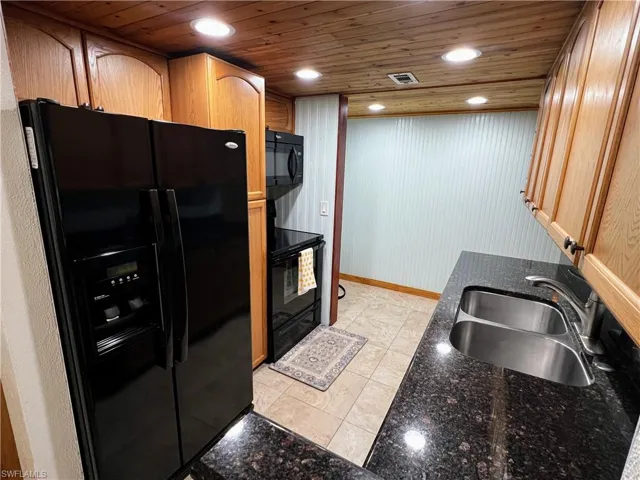Kitchen with dark stone countertops, black appliances, a sink, and wooden ceiling