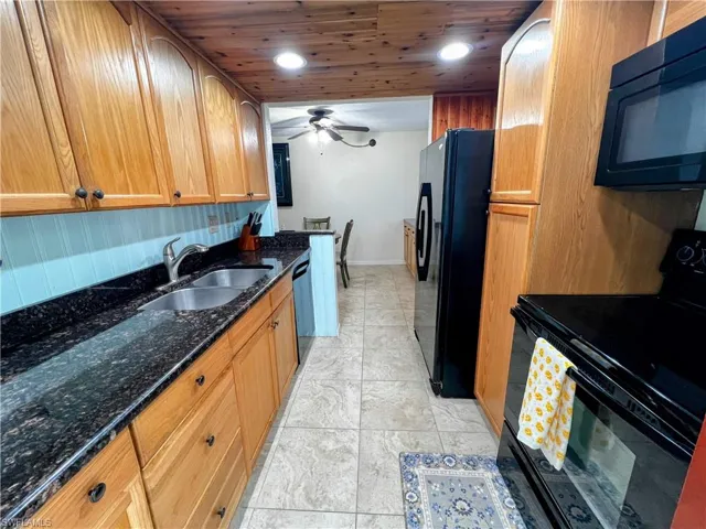 Kitchen featuring dark stone counters, black appliances, ceiling fan, a sink, and baseboards