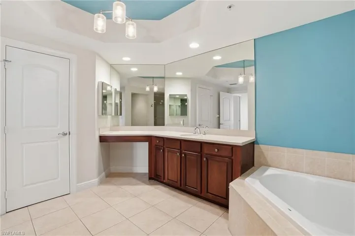 PrimaryBathroom with a tray ceiling, recessed lighting, vanity, light tile patterned flooring, and a bath