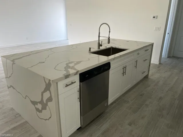 Kitchen featuring wood tiled floors, white cabinets, a kitchen island with sink, and light stone countertops