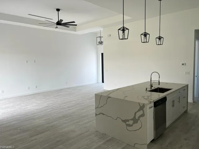 Kitchen featuring light stone counters, white cabinetry, open floor plan, an island with sink, and light wood-style floors