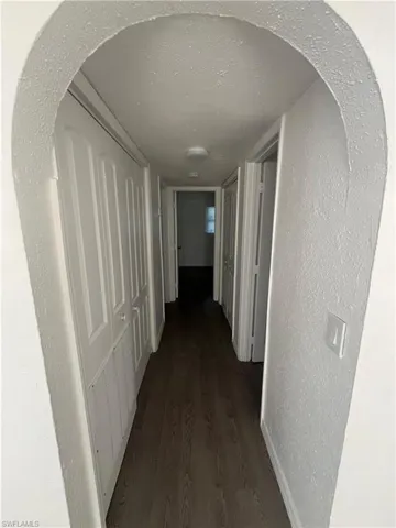 Hall featuring a textured wall, arched walkways, a textured ceiling, and dark wood-style floors