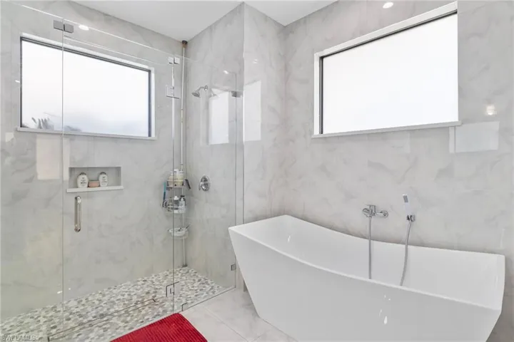 Bathroom with a freestanding tub, plenty of natural light, a marble finish shower, marble finish floors, and tile walls