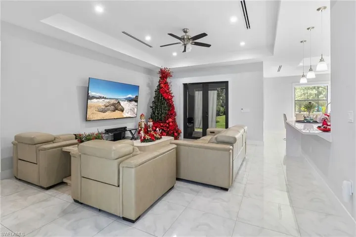 Living area featuring a raised ceiling, recessed lighting, french doors, a ceiling fan, and light marble finish flooring