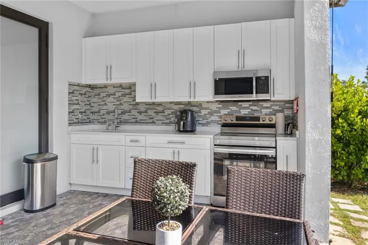 Kitchen with white cabinetry, stainless steel appliances, light stone countertops, and decorative backsplash