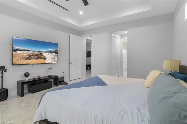 Bedroom featuring a raised ceiling, a ceiling fan, ensuite bath, a closet, and recessed lighting