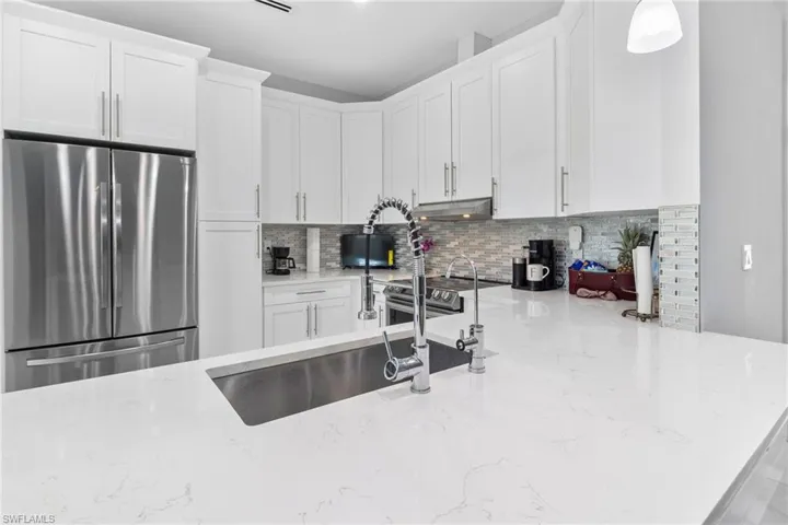 Kitchen with appliances with stainless steel finishes, light stone countertops, white cabinetry, tasteful backsplash, and pendant lighting