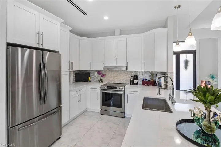 Kitchen featuring appliances with stainless steel finishes, white cabinets, light stone countertops, tasteful backsplash, and recessed lighting