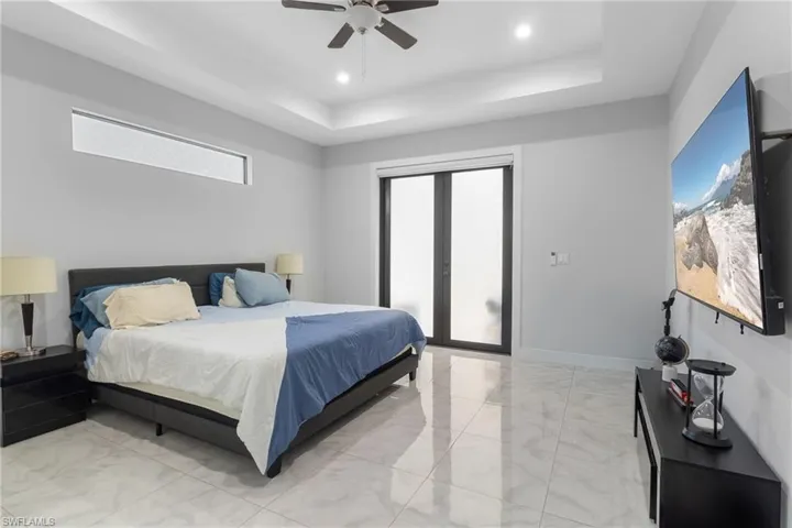 Bedroom with access to exterior, light marble finish floors, a tray ceiling, a ceiling fan, and recessed lighting