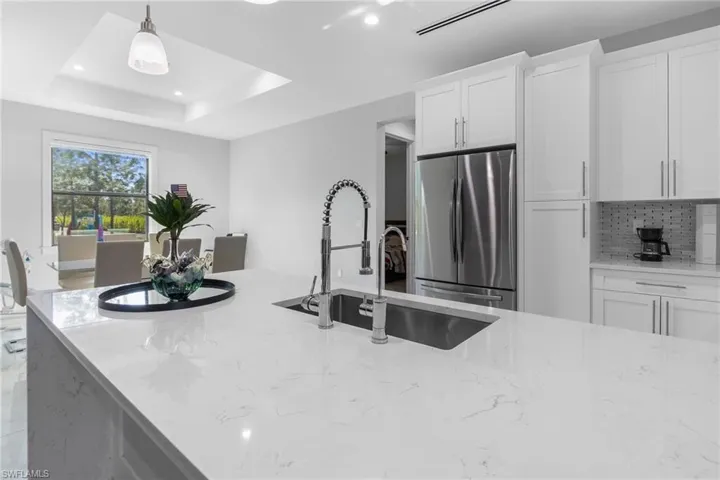 Kitchen with light stone counters, freestanding refrigerator, pendant lighting, white cabinets, and backsplash