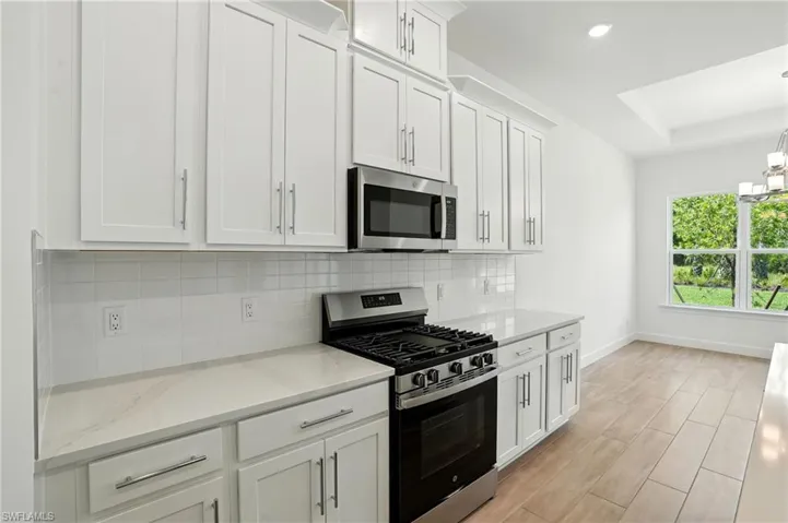 Kitchen featuring stainless steel appliances, white cabinets, tasteful backsplash, light stone countertops, and light wood finished floors