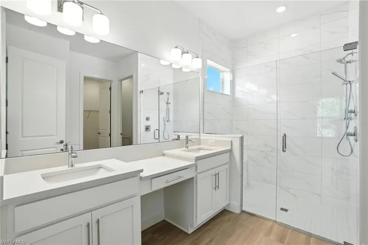 Bathroom with a spacious closet, a stall shower, double vanity, and light wood finished floors