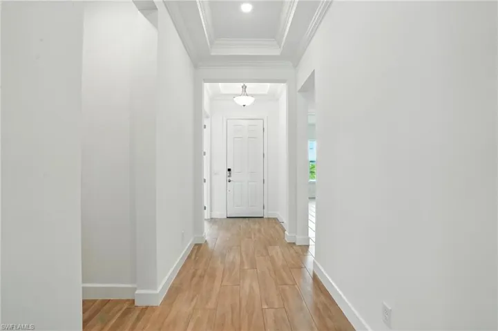 Hall featuring light wood-style flooring, ornamental molding, and a tray ceiling