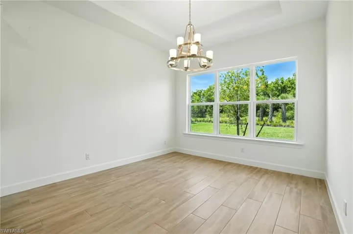 Unfurnished dining area featuring light wood-type flooring, a chandelier, and a raised ceiling