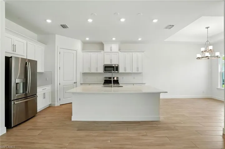 Kitchen with white cabinets, appliances with stainless steel finishes, light wood-type flooring, recessed lighting, and light stone counters