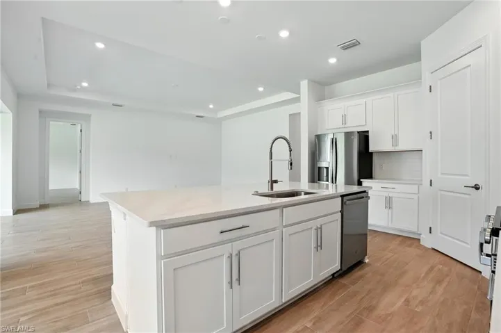 Kitchen featuring recessed lighting, wood finish floors, white cabinetry, a tray ceiling, and an island with sink
